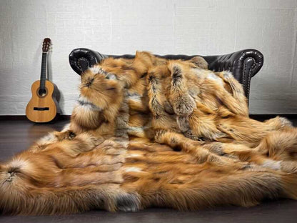 Fox Fur Blanket Throw Gold Saga Fox Natural - Tatifurs draped over a couch, showcasing vibrant orange and white fox fur.