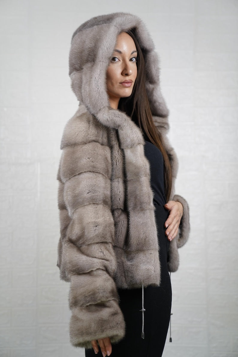 Woman wearing a gray mink fur coat with a hood against a plain background