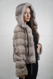 Woman wearing a gray mink fur coat with a hood against a plain background