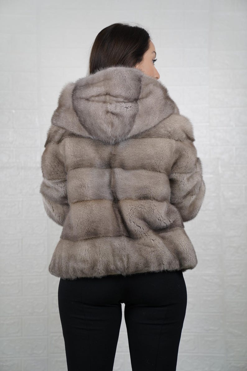 Person wearing a mink fur coat with a hood against a plain background