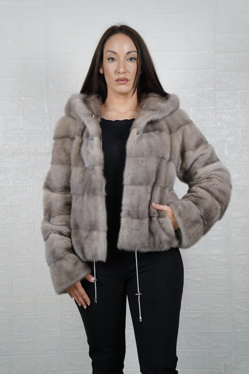 Woman wearing a mink gray fur coat against a white brick wall.