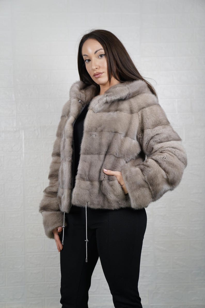 Woman wearing a mink gray fur coat against a plain background