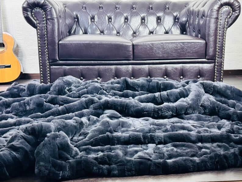 Rabbit Blanket Throw Rex Gray - Tatifurs draped on a floor in front of a tufted leather sofa.