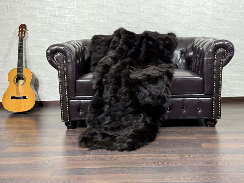 Fox Fur Blanket Throw Brown - Tatifurs elegantly draped on a brown leather sofa with a guitar in the background.