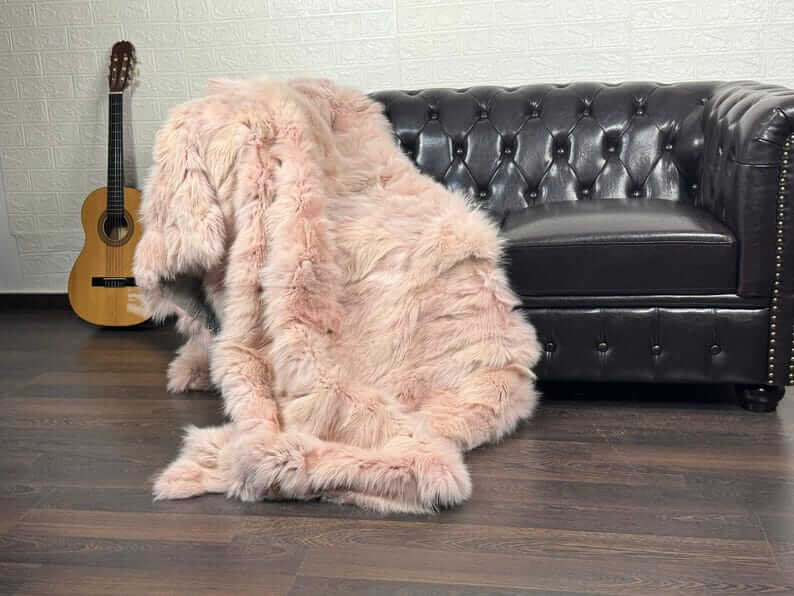 Fox Fur Blanket Throw Baby Pink - Tatifurs displayed on a black leather sofa, showcasing its softness and color.