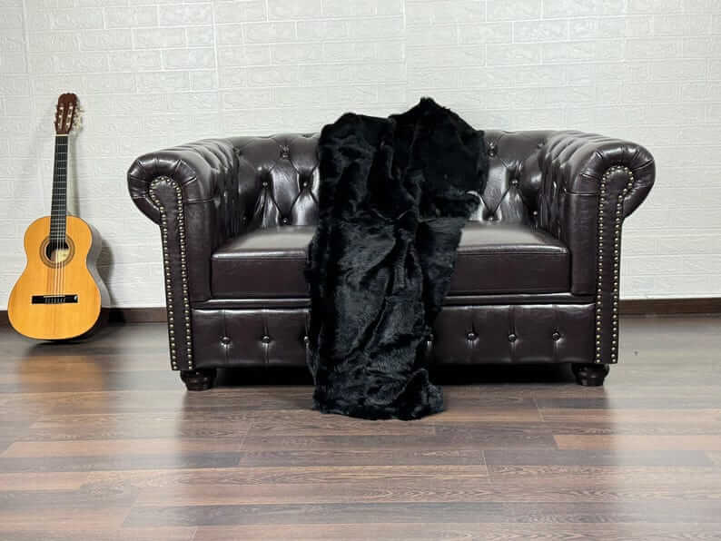 Rabbit Fur Blanket Throw Black - Tatifurs draped over a dark leather couch in a cozy living room setting.