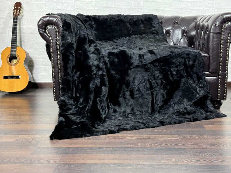 Rabbit Fur Blanket Throw Black - Tatifurs draped over a sofa, showcasing its luxurious softness and deep black color.