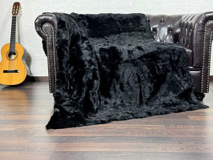 Rabbit Fur Blanket Throw Black - Tatifurs draped over a sofa, showcasing its luxurious softness and deep black color.