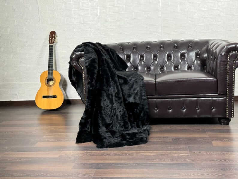 Rabbit Fur Blanket Throw Black - Tatifurs draped over a brown couch with a guitar nearby.