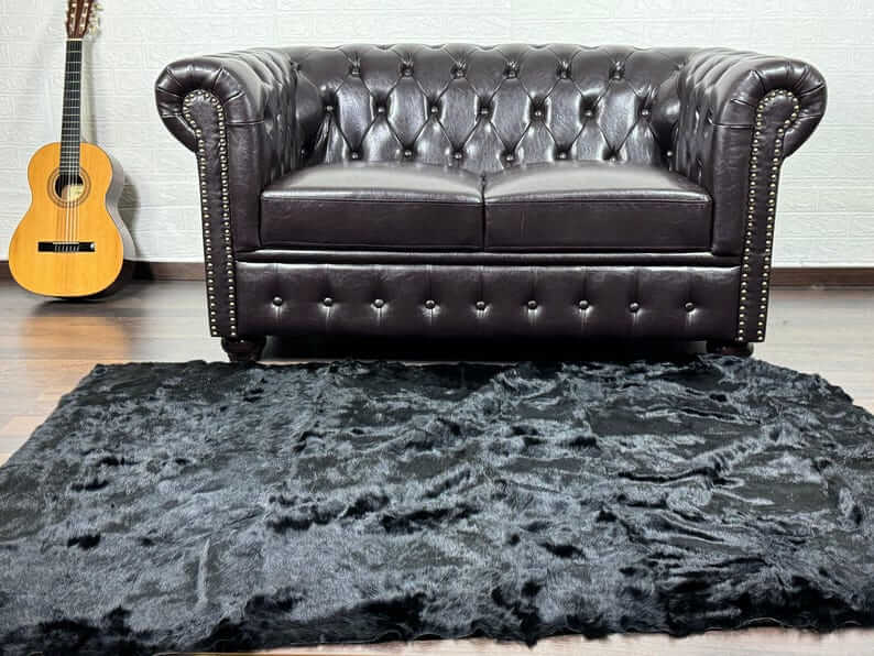 Rabbit Fur Blanket Throw Black - Tatifurs on a stylish living room floor with a leather sofa and guitar backdrop.