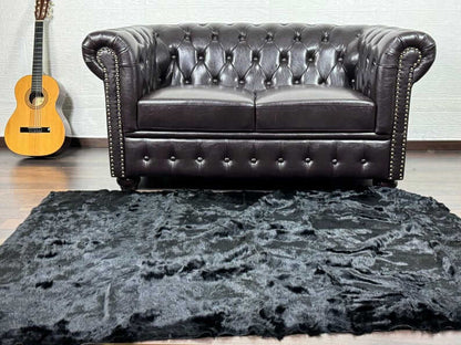 Rabbit Fur Blanket Throw Black - Tatifurs on a stylish living room floor with a leather sofa and guitar backdrop.