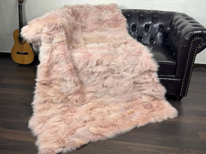 Fox Fur Blanket Throw Baby Pink - Tatifurs draped over a black leather couch with a guitar in the background.