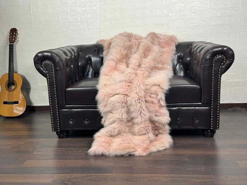 Fox Fur Blanket Throw Baby Pink - Tatifurs draped over a stylish black leather couch, showcasing its softness and elegant color.