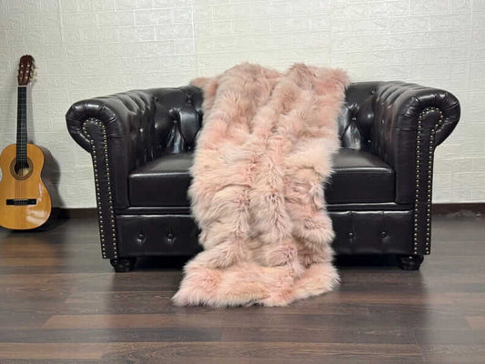Luxury baby pink fox fur blanket draped over a bed showing soft pale pink tones and natural fur volume
