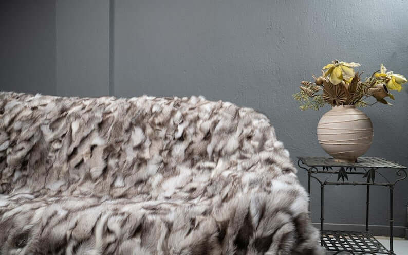 Fox Fur Blanket Throw Blue Natural Dark - Tatifurs displayed on a couch with decorative vase and flowers.