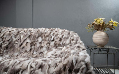 Fox Fur Blanket Throw Blue Natural Dark - Tatifurs displayed on a couch with decorative vase and flowers.