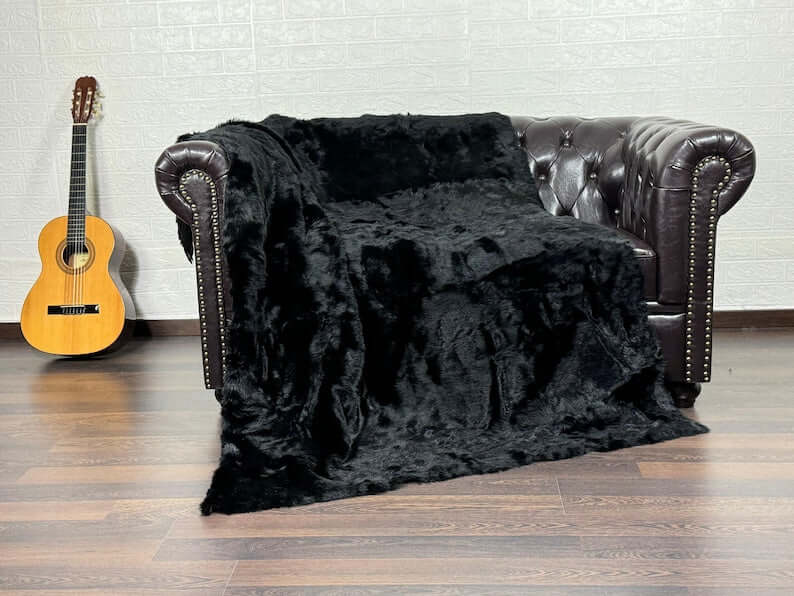 Rabbit Fur Blanket Throw Black - Tatifurs draped over a dark leather couch with a guitar in the background.