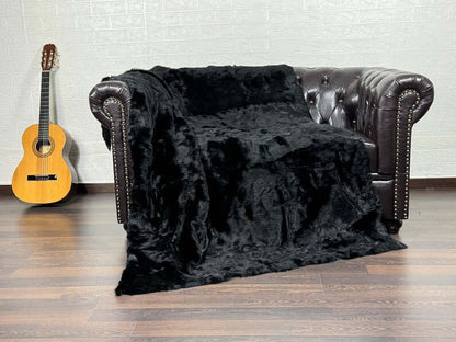 Rabbit Fur Blanket Throw Black - Tatifurs draped over a dark leather couch with a guitar in the background.