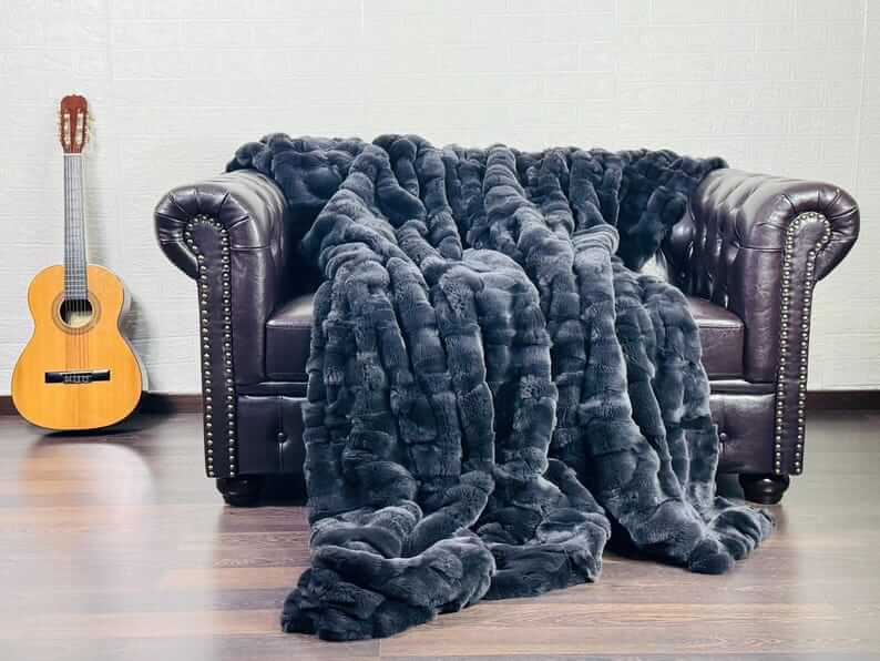 Rabbit Blanket Throw Rex Gray - Tatifurs draped over a dark leather couch beside an acoustic guitar.
