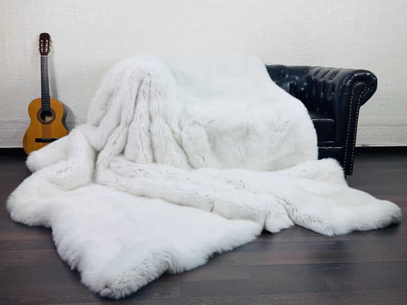 White Fox Fur Throw Blanket - Tatifurs draped over a black sofa with an acoustic guitar in the background.