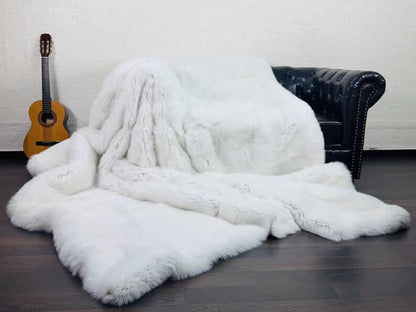 White Fox Fur Throw Blanket - Tatifurs draped over a black sofa with an acoustic guitar in the background.