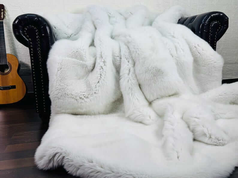 White Fox Fur Throw Blanket - Tatifurs displayed on a stylish black couch, showcasing its luxurious, pristine texture.