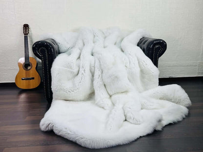 White Fox Fur Throw Blanket - Tatifurs draped on a black couch with a guitar in the background, showcasing its luxurious texture.
