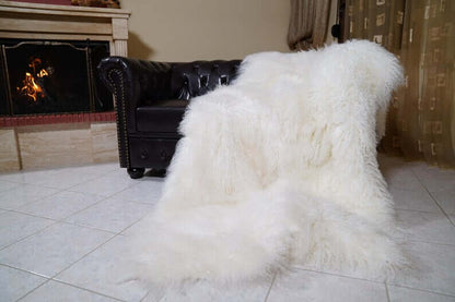 White Wool Sheepskin Mongolian Blanket Throw - Tatifurs elegantly draped on a leather couch next to a fireplace.