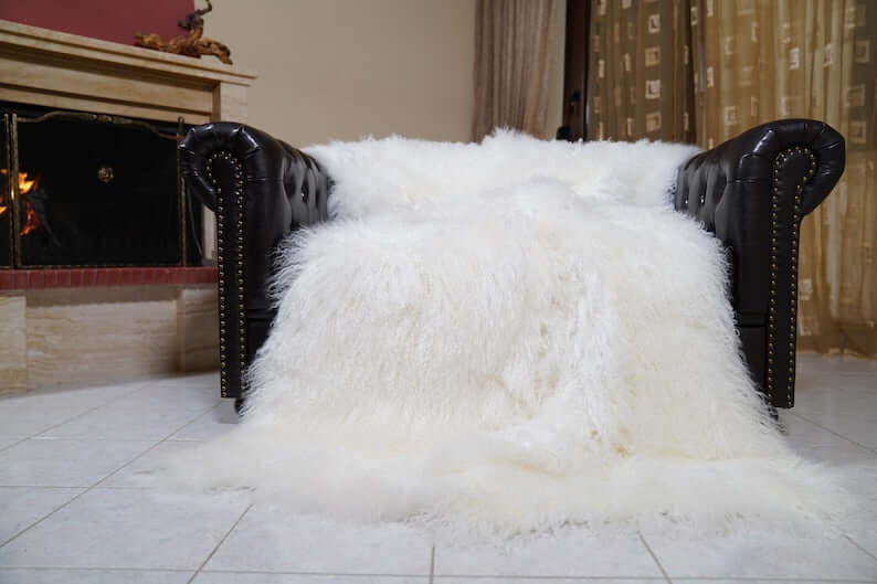 White Wool Sheepskin Mongolian Blanket Throw - Tatifurs draped on a leather couch in a cozy living room setting.