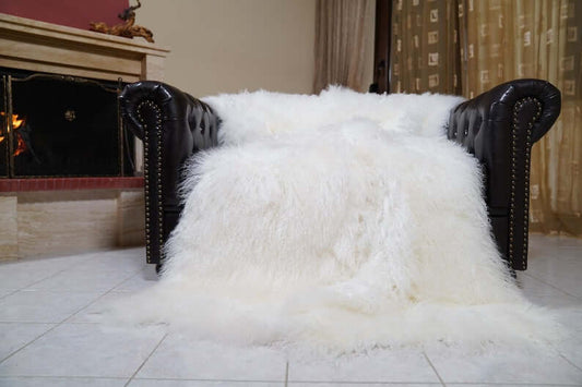 White fur rug on a black leather chair in a room with a fireplace and patterned wallpaper.