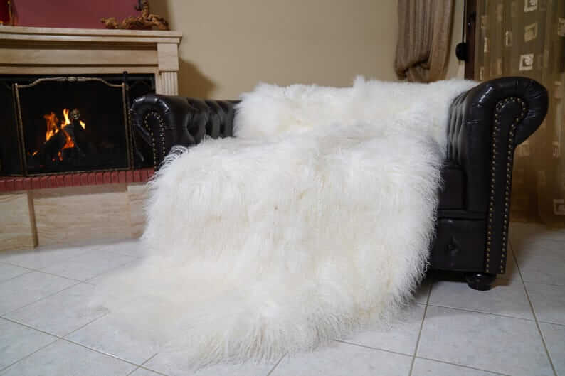 White Wool Sheepskin Mongolian Blanket Throw - Tatifurs draped over a black leather couch by a fireplace.