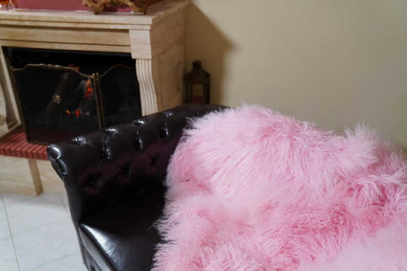 Wool Sheepskin Mongolian Blanket Throw Pink - Tatifurs draped over a black leather chair near a fireplace.