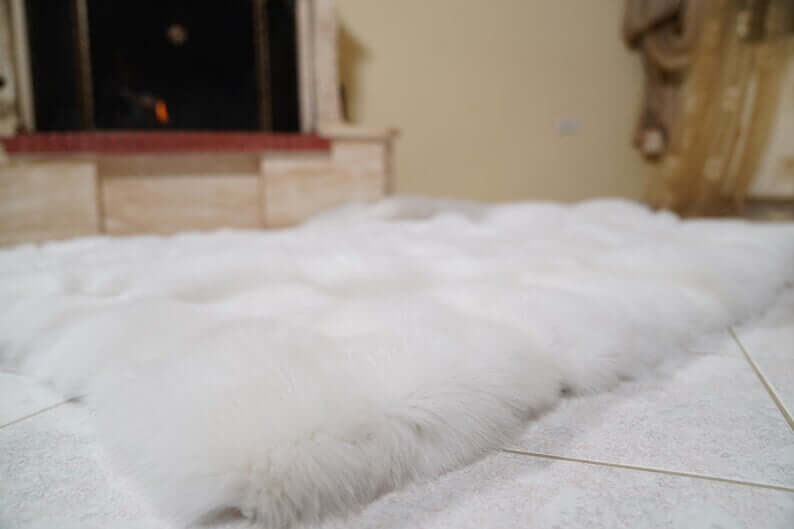 White Wool Sheepskin Mongolian Blanket Throw - Tatifurs on a floor near a fireplace, showcasing its soft, fluffy texture.