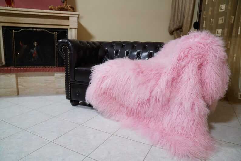Wool Sheepskin Mongolian Blanket Throw Pink - Tatifurs draped on a black leather couch in a cozy living room.