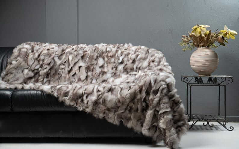Fox Fur Blanket Throw Blue Natural Dark - Tatifurs displayed on a black sofa with a vase and flowers.