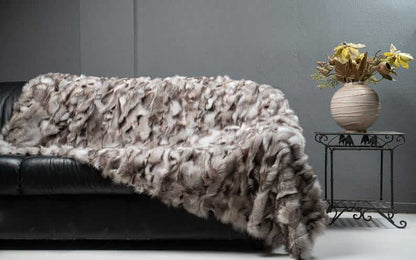 Fox Fur Blanket Throw Blue Natural Dark - Tatifurs displayed on a black sofa with a vase and flowers.