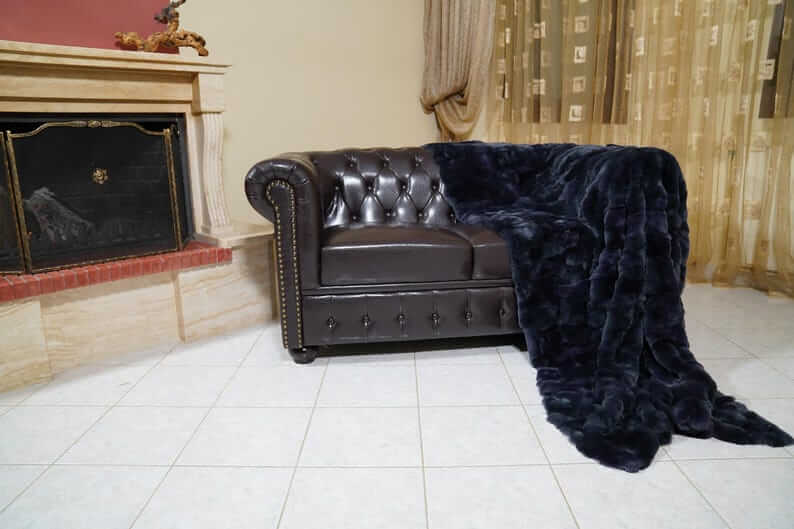Double Sided Fur Rex Rabbit Blanket Throw Dark Blue draped over a luxurious brown leather couch.