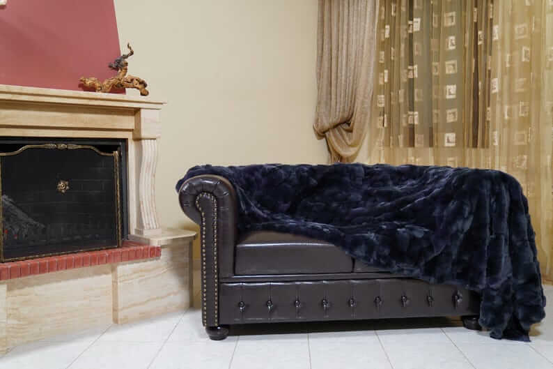 Double Sided Fur Rex Rabbit Blanket Throw Dark Blue draped over a stylish leather couch in a cozy living room setting.
