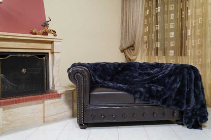 Double Sided Fur Rex Rabbit Blanket Throw Dark Blue draped over a stylish leather couch in a cozy living room setting.