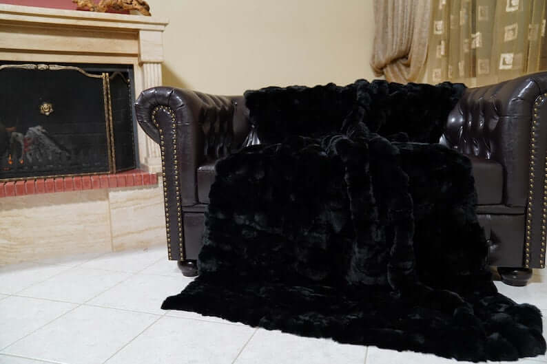Rabbit Blanket Throw Rex Black - Tatifurs displayed on a stylish leather couch near a fireplace.