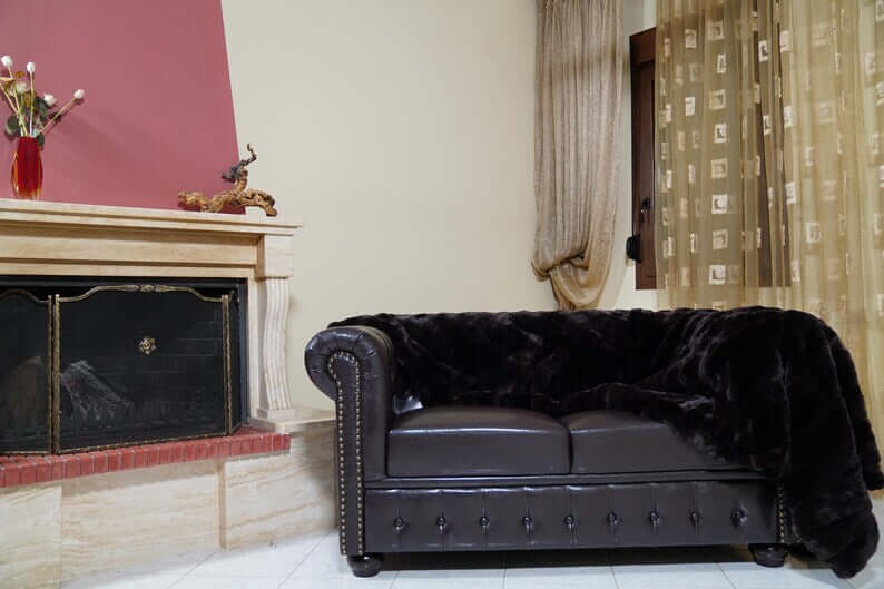 Rabbit Blanket Throw Rex Dark Brown - Tatifurs draped over a luxurious brown leather sofa in an elegant living room.