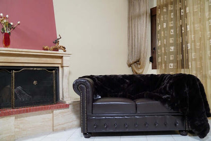 Rabbit Blanket Throw Rex Dark Brown - Tatifurs draped over a luxurious brown leather sofa in an elegant living room.