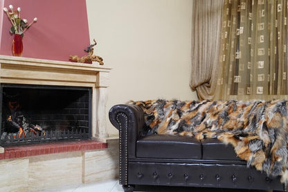 Fur Throw Blanket Natural Gross Fox – Luxury - Tatifurs displayed on a dark couch near a fireplace in a cozy living room.