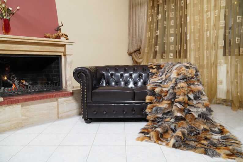 Fur Throw Blanket Natural Gross Fox – Luxury - Tatifurs draped over a black leather sofa by a fireplace.
