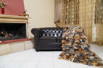 Fur Throw Blanket Natural Gross Fox – Luxury - Tatifurs draped over a black leather sofa by a fireplace.