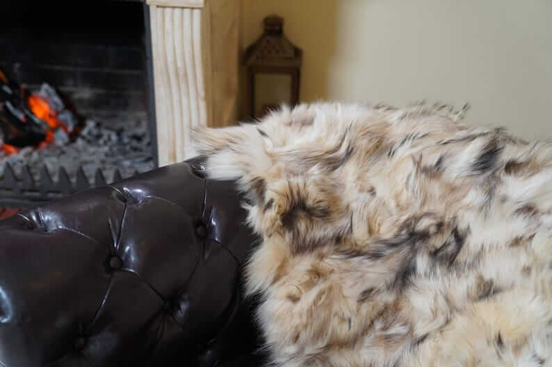 Fox Fur Blanket Throw Double Sided Iceberg Beige draped over a leather chair near a cozy fireplace.