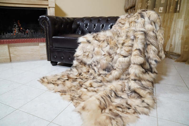 Fox Fur Blanket Throw Double Sided Iceberg Beige draped over a leather sofa near a fireplace in a cozy living room.