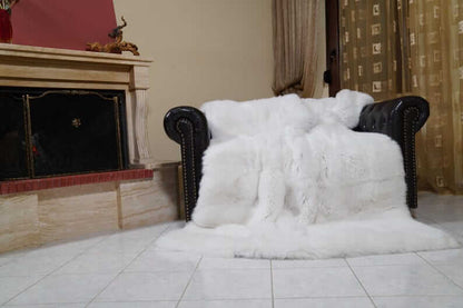 White Fox Fur Throw Blanket - Tatifurs draped on a stylish black leather couch in a cozy setting.