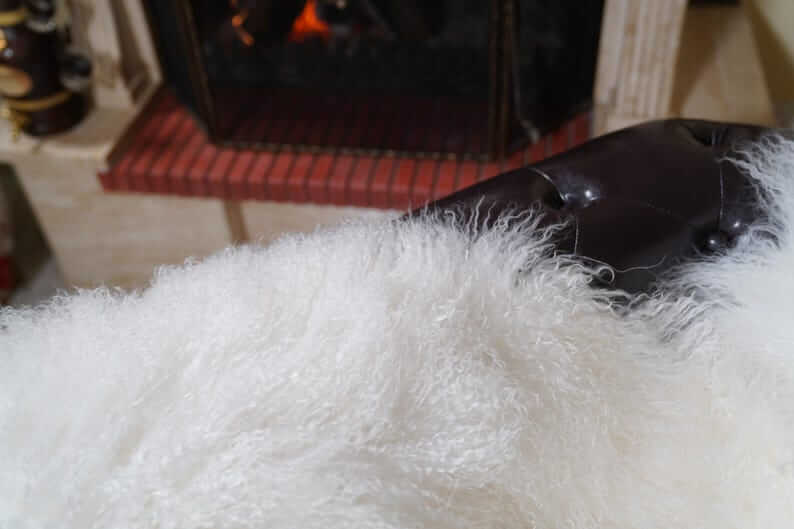 White Wool Sheepskin Mongolian Blanket Throw - Tatifurs displayed on a cozy sofa near a fireplace with a warming ambiance.