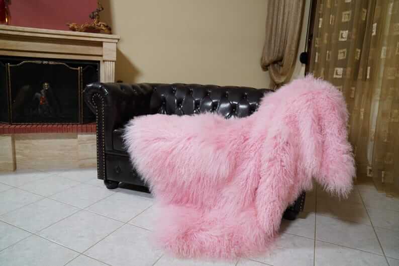 Wool Sheepskin Mongolian Blanket Throw Pink - Tatifurs draped over a black leather sofa, showcasing its fluffy pink texture.